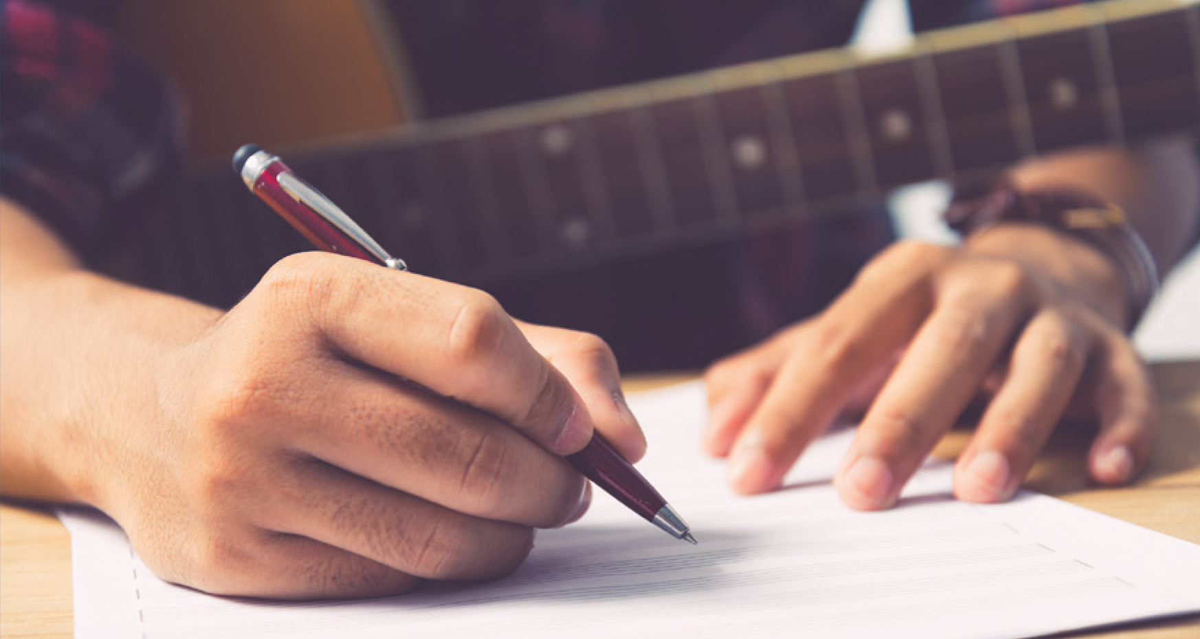 Musician holding guitar; writing notation with pen